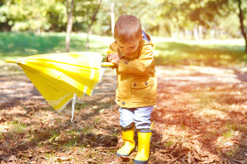 Cute toddler boy in yellow rubber boots, yellow raincoat holding a yellow lemon umbrella in an...