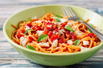 Spaghetti pasta with tomato sauce, mozzarella cheese and fresh basil leaves on white-blue vintage wooden background. Selective focus.