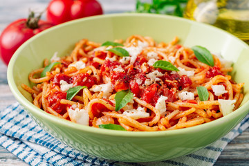 Spaghetti pasta with tomato sauce, mozzarella cheese and fresh basil leaves on white-blue vintage wooden background. Selective focus.