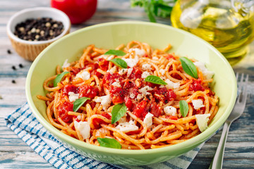 Spaghetti pasta with tomato sauce, mozzarella cheese and fresh basil leaves on white-blue vintage wooden background. Selective focus.