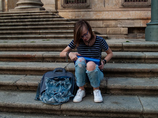 A teenage woman studying with a binder on the stairs of a university in a university campus