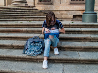 A teenage woman studying with a binder on the stairs of a university in a university campus