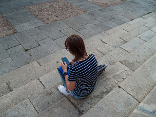 A teenage woman with a smart phone on her hands on the stairs of an historial building