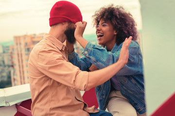 Funny game. Funny playful young girl laughing while pulling red hat of her boyfriend up to his nose