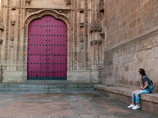 A teenage woman sitting in front of a wall and looking at the door of a cathedral