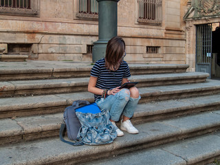 A teenage woman with a tablet on the stairs of a university in a university campus