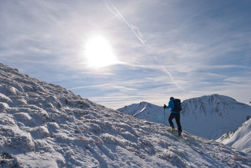 Mountaineer climbs a mountain, which is nearly free of snow by the wind. The sun is shining through...