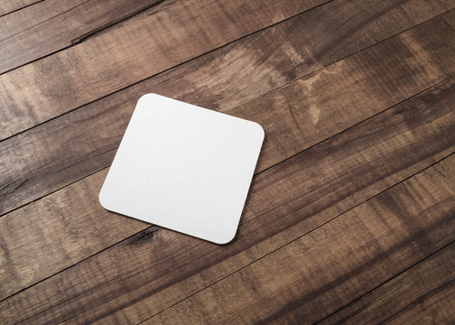 Blank square beer coaster on wooden background.