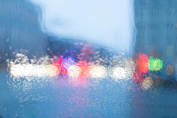Bokeh from illumination of fires of the night city through glass of the car and a rain. Drops of a rain flow down on glass. Indistinct focus