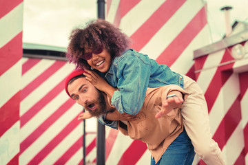 Obraz premium Closing ears. Cheerful happy young woman laughing and closing the ears of her boyfriend while sitting on his back