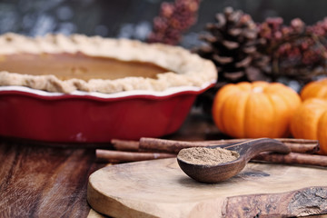 Fototapeta na wymiar Pumpkin pie spice measured in a wooden spoon over a rustic wooden background. Pie and pumpkins in the background. Blurred background with selective focus on spice.