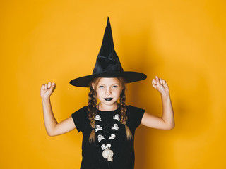young halloween witch on orange background with black hat