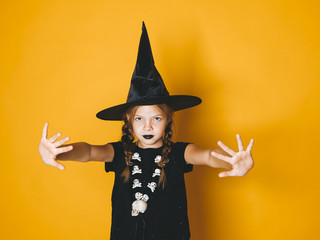 young halloween witch on orange background with black hat