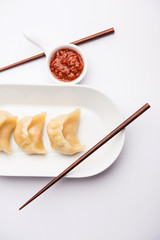 Dumpling momos food from Nepal or Ladakh served with red chilli chutney over moody background. Selective focus