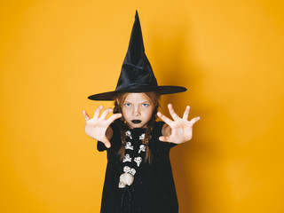 young halloween witch on orange background with black hat