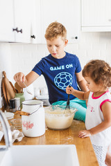 Brother and sister preparing dough for pancakes at the kitchen.