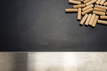 A lot of wooden pegs and hand saw for wood lying flat on a black background.