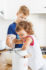 Brother and sister preparing dough for pancakes at the kitchen.