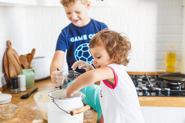 Brother and sister preparing dough for pancakes at the kitchen.