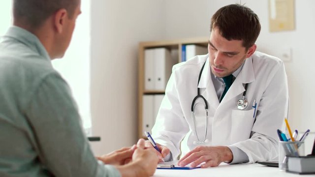 medicine, healthcare and people concept - doctor writing prescription for male patient at clinic
