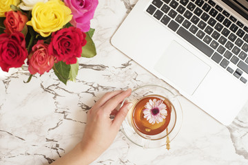 Feminine workplace concept. Freelance workspace in flat lay style with laptop, tea, flowers. Woman...