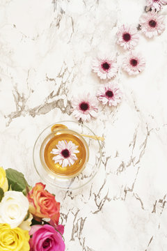 A cup of healthy herbal tea. Beautiful fresh flowers on light marble table, top view. Pink bouquet on a female work desk. Blogger lifestyle. Floral frame