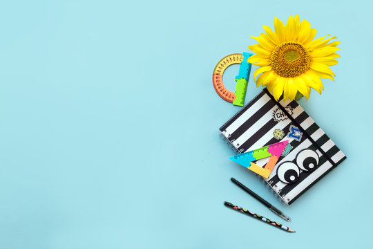 School accessories striped black and white notebook, pen, pencile and sunflower on blue background, spiral notepad on a table. Back to school, Still life, business, office, education concept, mock up