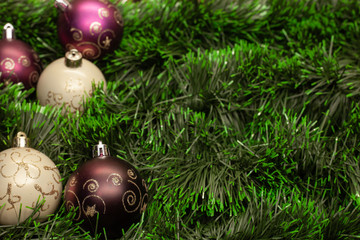 Christmas toy white ball and purple ball with patterns on green tinsel on a wooden background