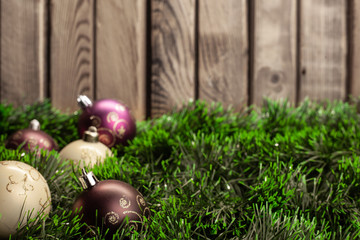 Christmas toy white ball and purple ball with patterns on green tinsel on a wooden background