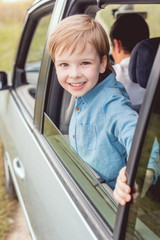 happy little kid riding car with his dad on nature and looking at camera
