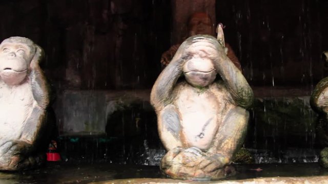 Monkey statues Hear no evil, speak no evil, see no evil in Buddhist shrine with water falling in background.