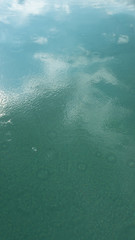 Kräuselungen von Wassertropfen, Kreise auf Türkis blauem Wasser, Spiegelung, Reflexion von Wolken und blauem Himmel,Pool, abstrakter Hintergrund, verwischt.mit Raum für Text.