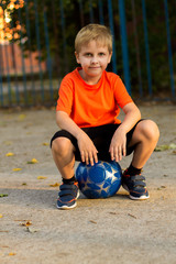 the boy, a student in an orange shirt playing soccer on the Playground