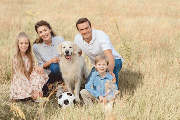happy young family with retriever dog sitting in field together and looking at camera