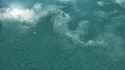 Undeutliche Wassertropfen und Kreise auf blauer Swimmingpool-Wasseroberfläche, abstrakter Wasserhintergrund, Spiegelung, Reflexion von Wolken und blauem Himmel,Pool, mit Raum für Text