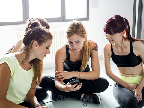 female friends in locker room of the gym relaxing looking at a smartphone and chatting