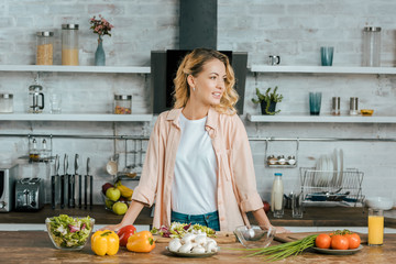 attractive young woman with various ripe vegetables on table looking away at kitchen