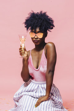 Cool girl with sunglasses holding champagne glass, isolated on pink