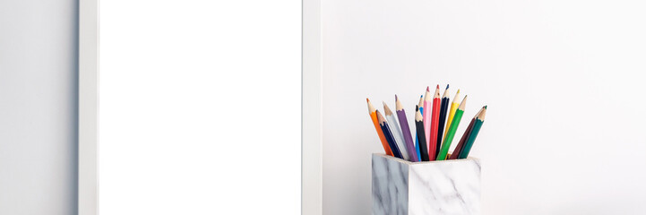 Fototapeta premium Panoramic photo with a white mockup frame and colored pencils in a marble container