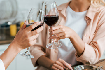 cropped shot of women clinking with glasses of red wine