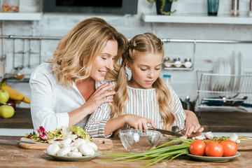 happy adult mother teaching her little daughter how to cook