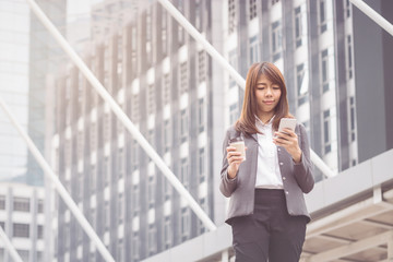 Businesswoman using smart phone and drinking hot coffee in the morning at ueban background