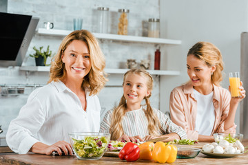 adult woman cutting vegetables for salad with daughter and granddaughter at home