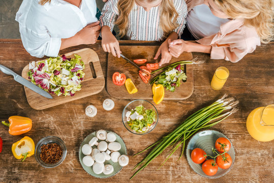 Cropped Shot Of Child Cutting Vegetables For Salad With Mother And Grandmother At Home