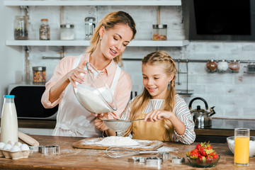 happy mother and daughter pouring flour through sieve for dough at kitchen