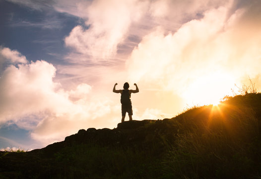 People, power, strength, and determination.  Strong male hiker flexing his muscles on a mountain at sunset.