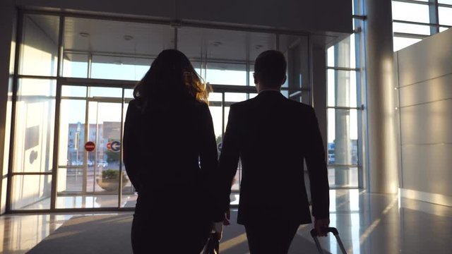 Business man and woman with luggage going from the airport to city street. Follow to young businessman carrying suitcase on wheels and walking with his female colleague from terminal hall. Slow motion