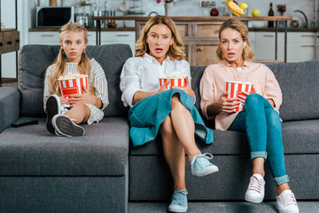 shocked child with mother and grandmother watching movie on couch at home with buckets of popcorn