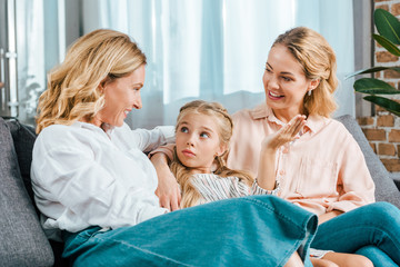 happy child with mother and grandmother sitting on couch at home