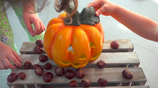 Little girl playing feeding chestnuts to halloween pumpkin, child play, holiday decoration, unrecognizable